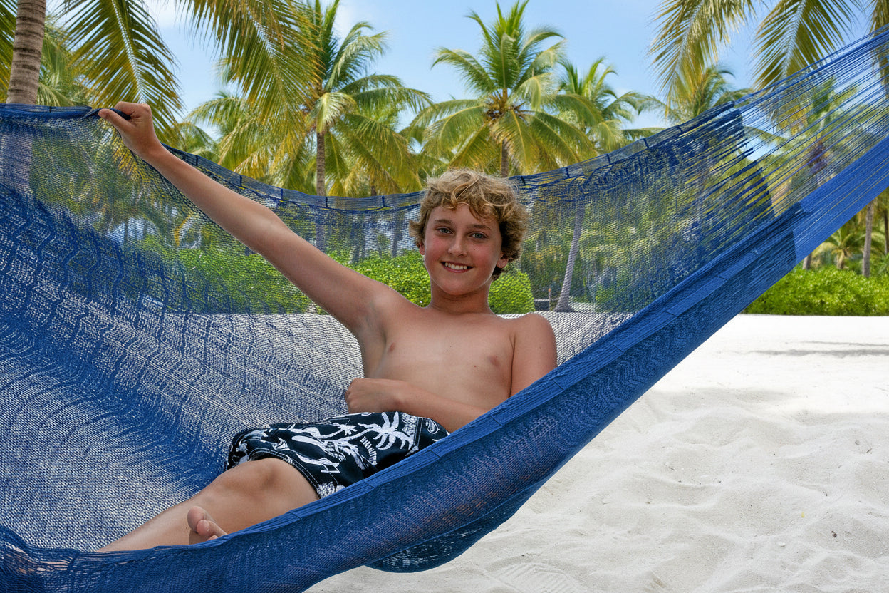 Junge liegt am Palmenstrand in Hängematte Mexi 2 und hält diese auf, so dass man die Struktur gut sieht